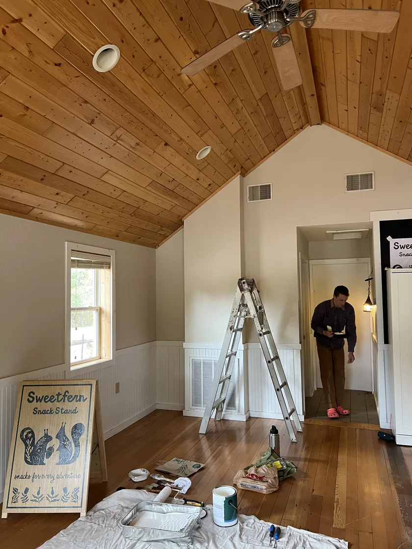 Inside the future shack: a ladder, paint, and the market sign against the wall.